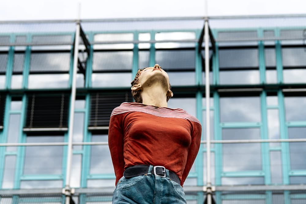 The very first column saint, “Marlis,” by artist Christoph Pöggeler, looks up at the Rhine Tower in Düsseldorf. She stands on Stromstraße near the WDR building. 